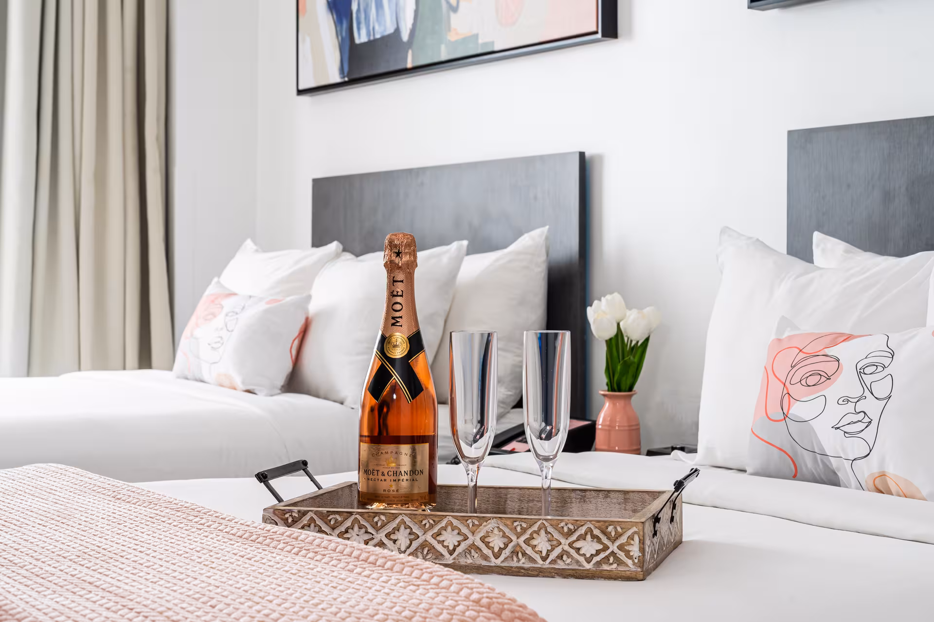 A hotel room with two beds, champagne, and pink accents.