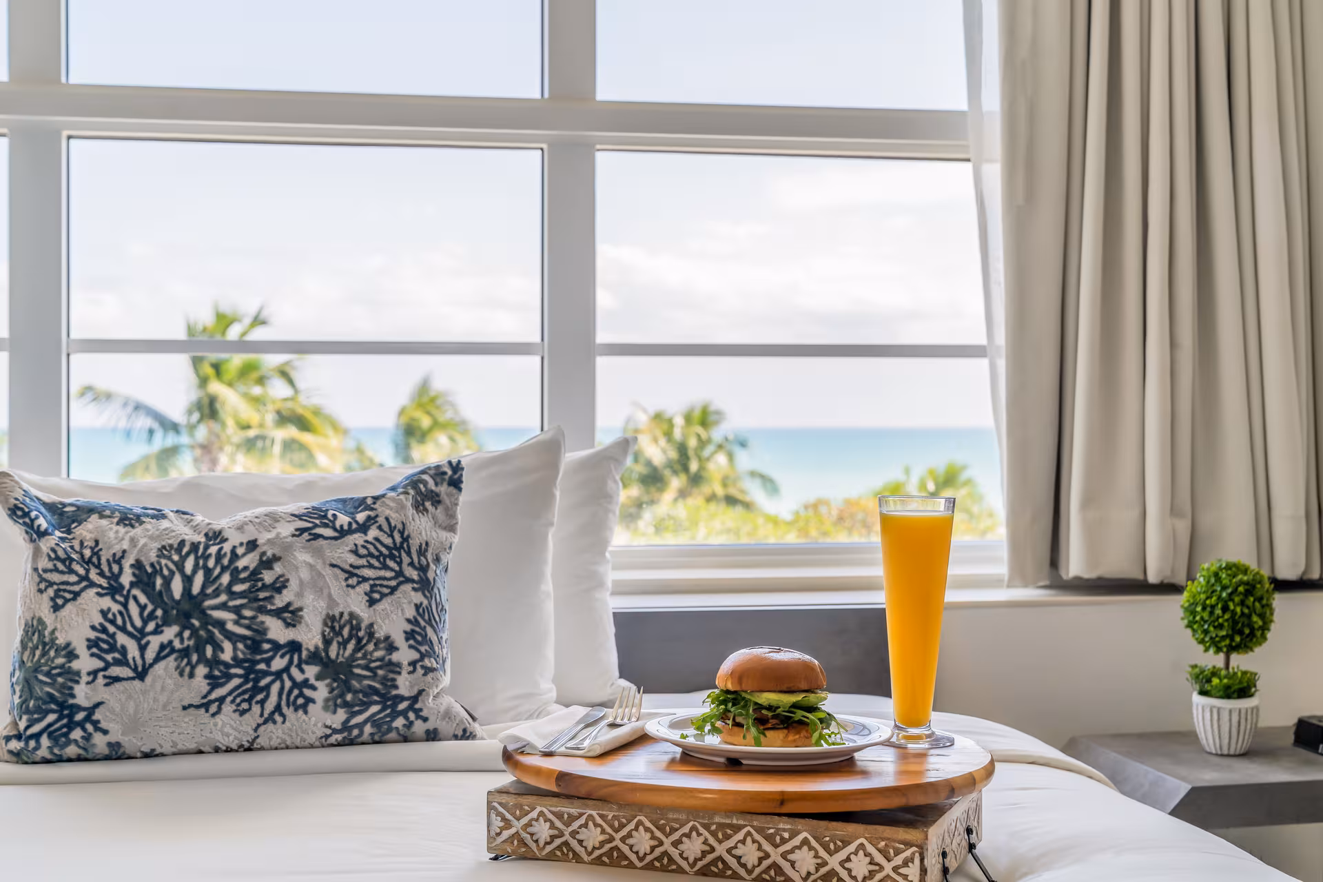 A bed with a tray of food and drink in front of a window with an ocean view
